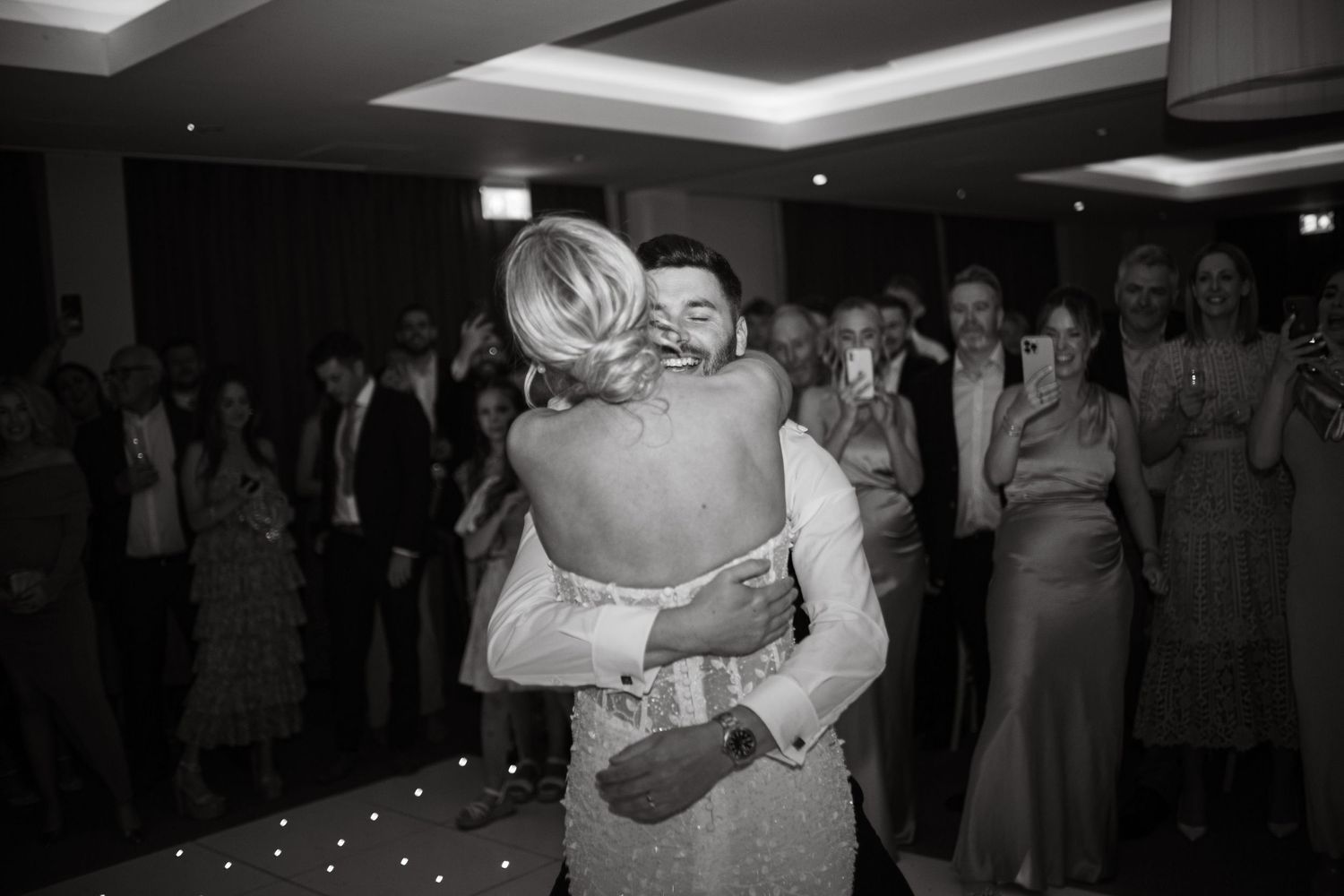 Wedding guests gather around the dance floor during an evening reception celebration.