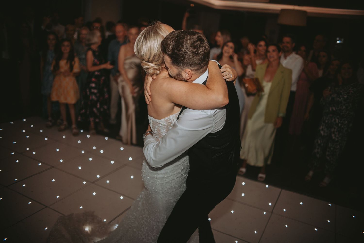 Couples share intimate dances during an evening wedding reception with twinkling lights overhead.