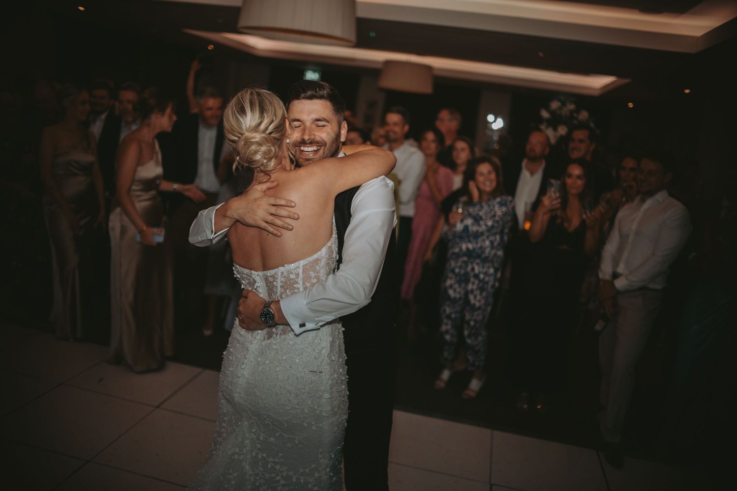 Newlyweds share their first dance at a wedding reception while guests watch in the background.