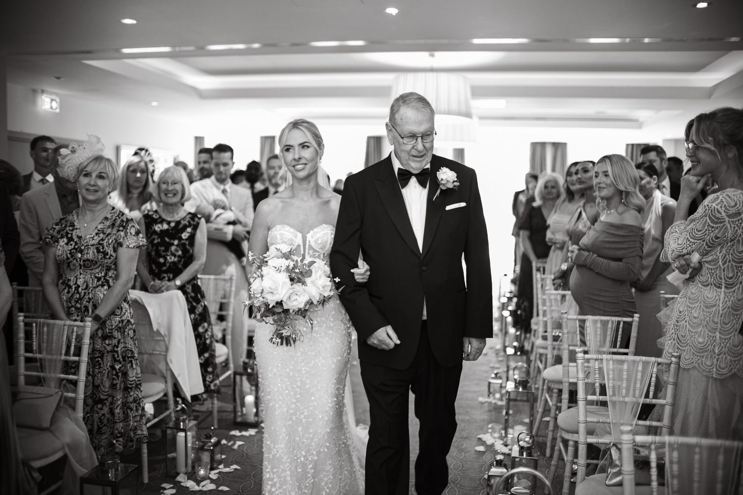 Wedding ceremony guests seated in white chairs inside an elegant reception venue.