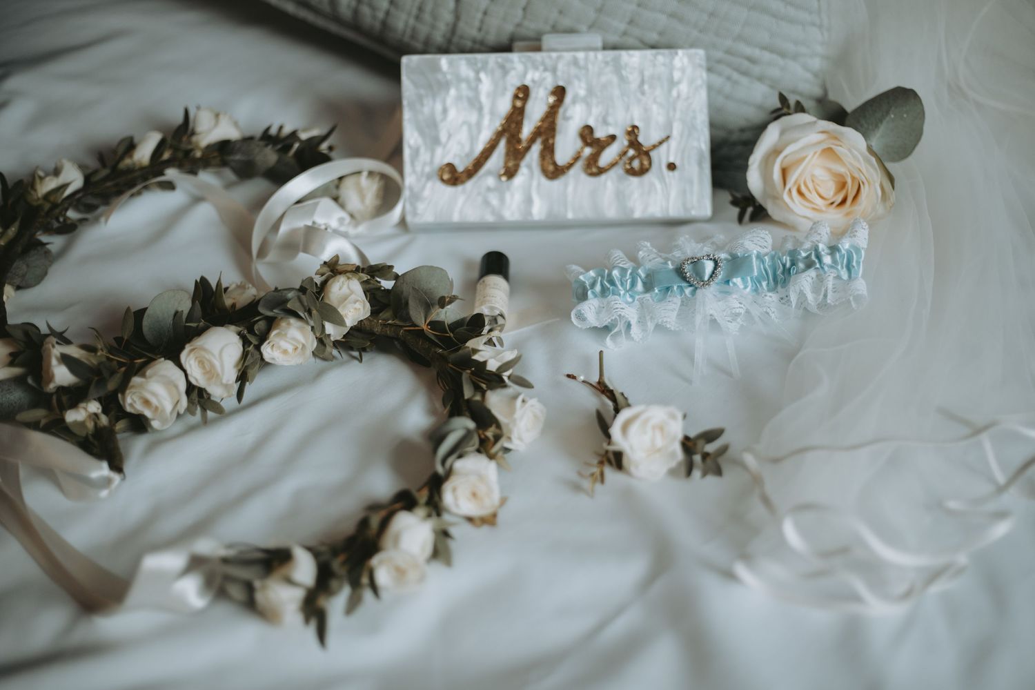 Wedding details with 'Mrs.' sign and floral crown on white fabric.