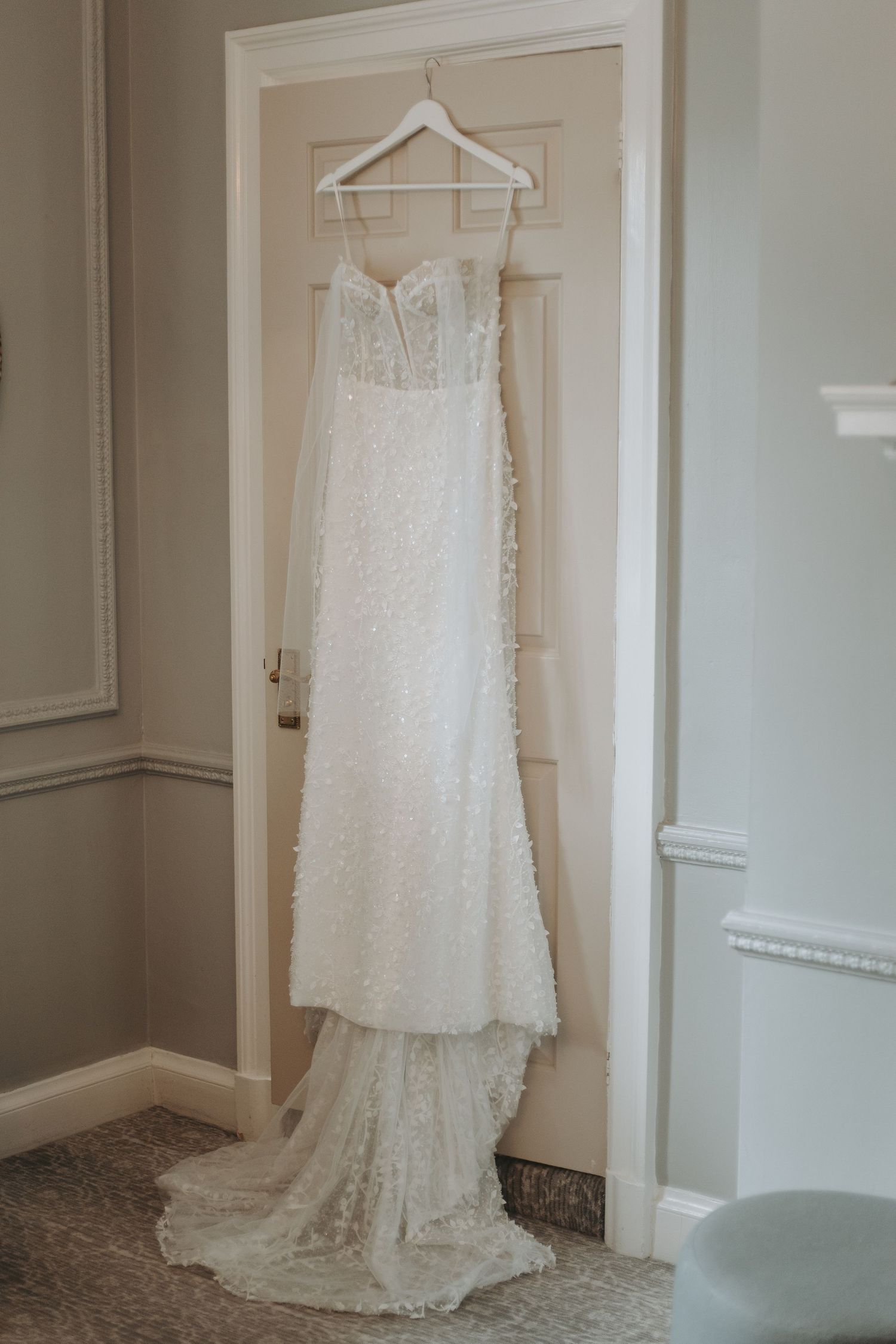 Elegant lace wedding dress hanging on white door with long train flowing down.