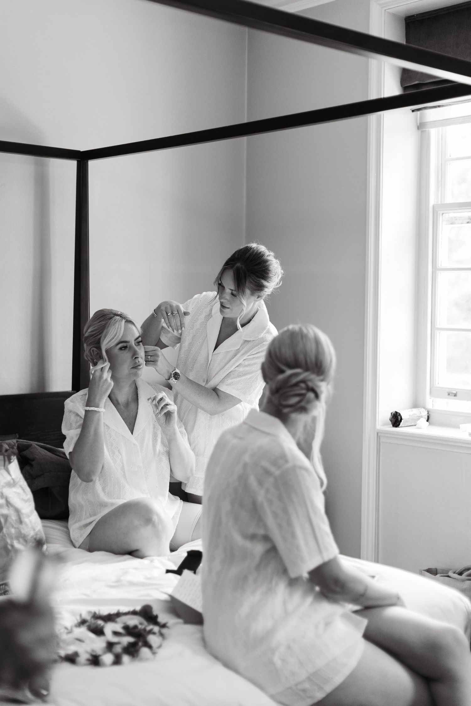 Wedding preparation scene with people in white getting ready on a bed.