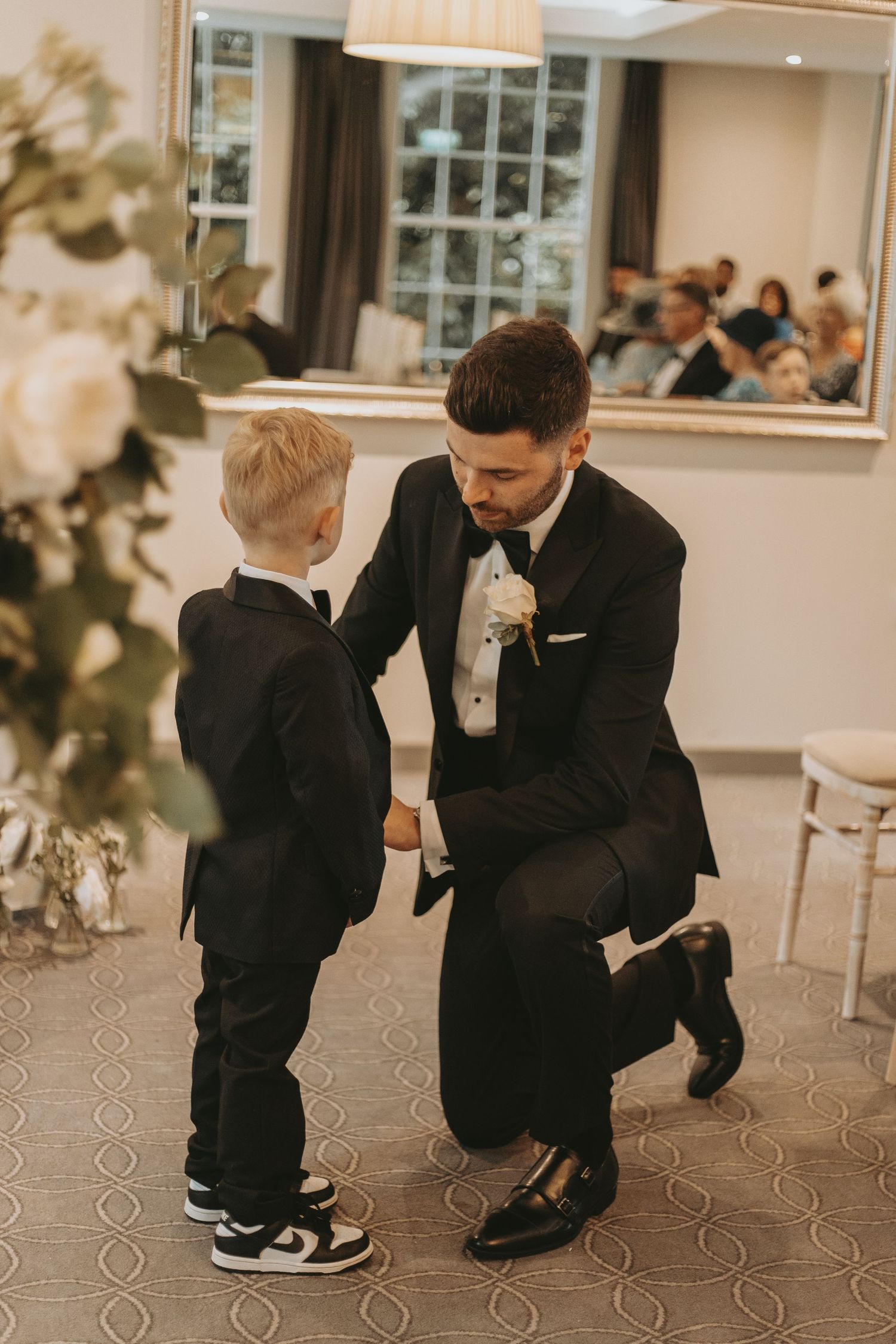 A touching moment between a groom and young attendee in formal attire on a patterned carpet.