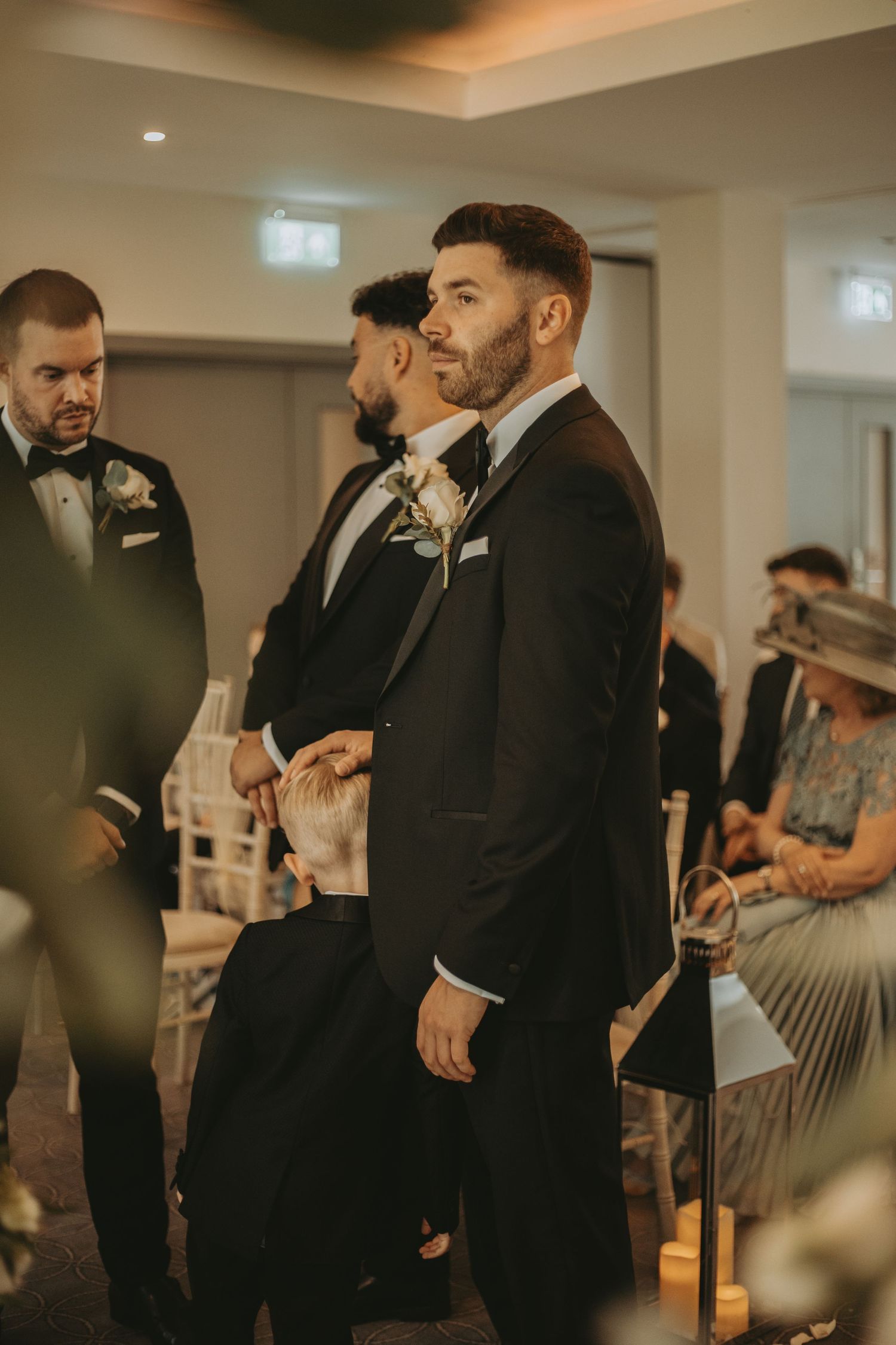 Wedding party members in black tuxedos gather during an indoor celebration.