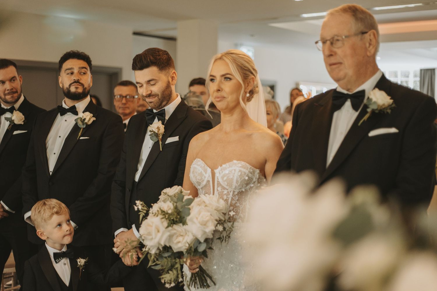 Wedding ceremony guests stand together in formal attire surrounded by elegant decor.