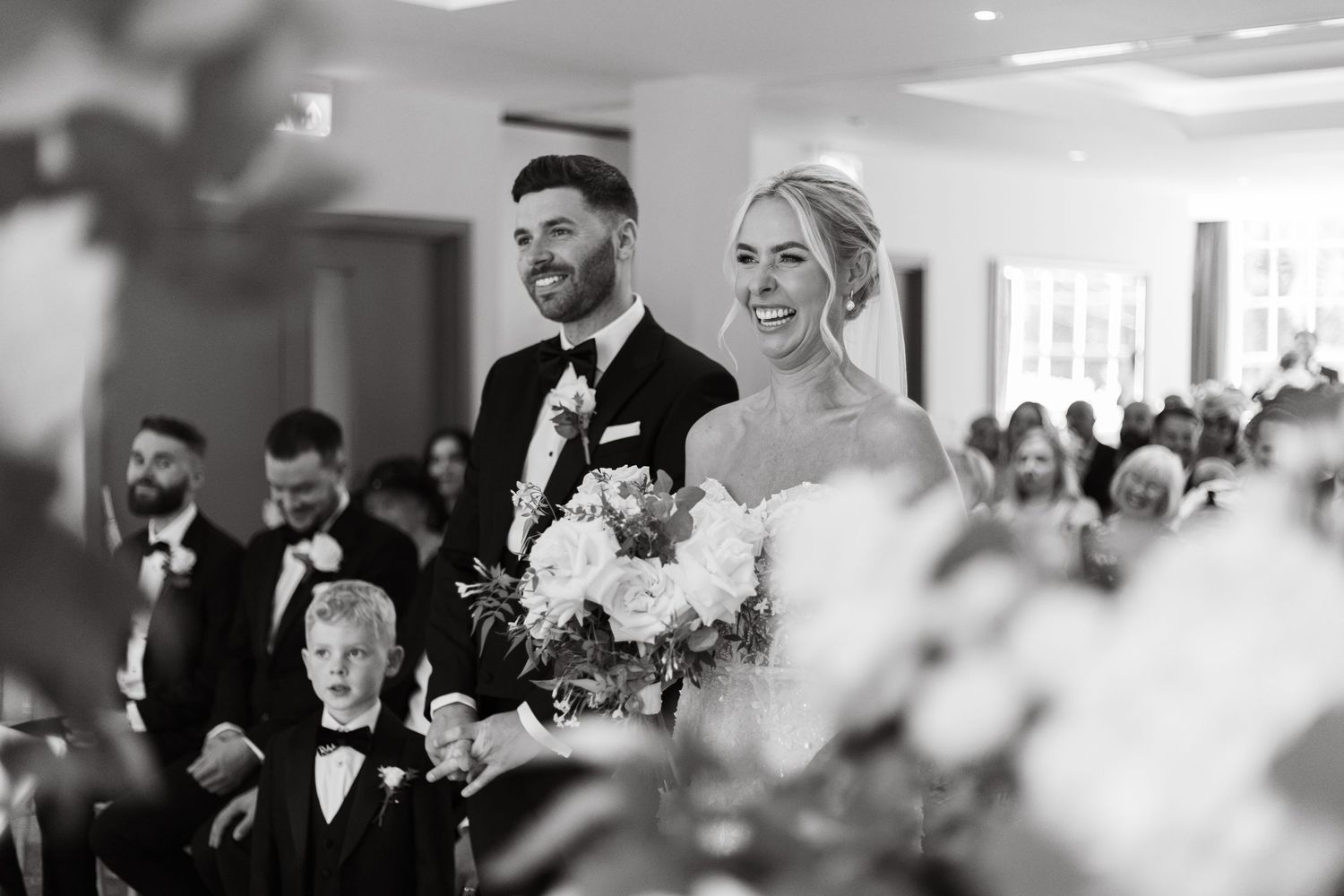 Black and white photo of wedding celebration with guests sharing joyful moments.