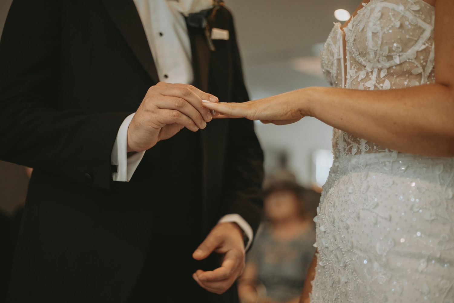 Close-up of hands exchanging rings during wedding ceremony with sparkly dress detail.