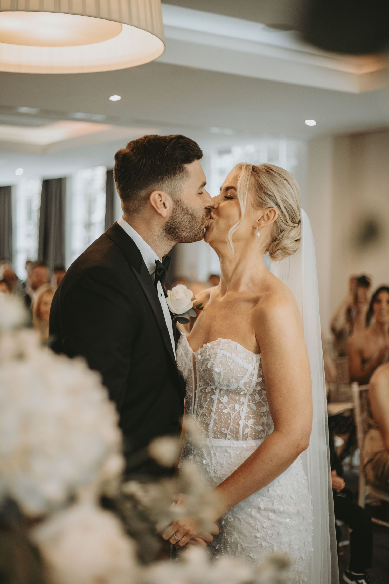Newlyweds share an intimate kiss during their wedding reception in an elegant indoor venue.