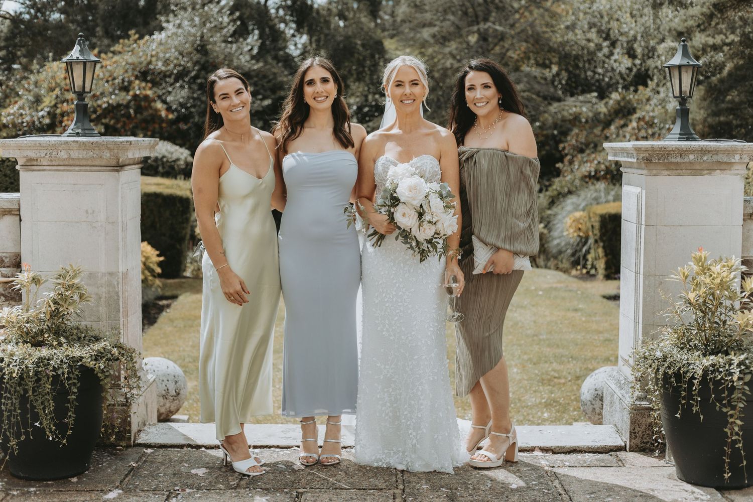 Bridesmaids in light blue and neutral dresses pose together outdoors at a garden wedding.