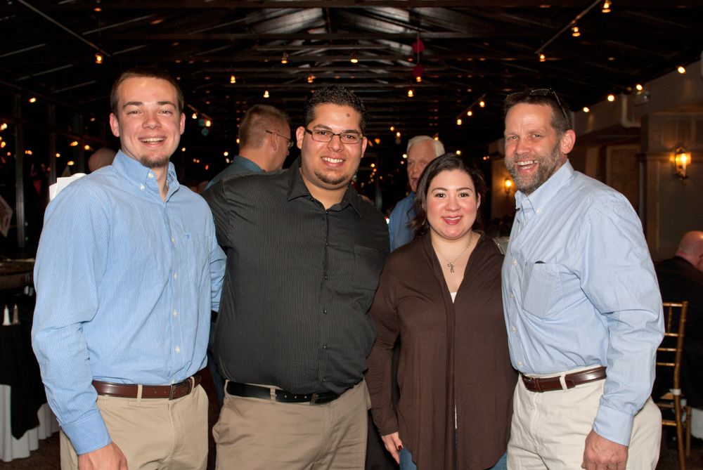 Four colleagues in business casual attire pose together at an indoor event.
