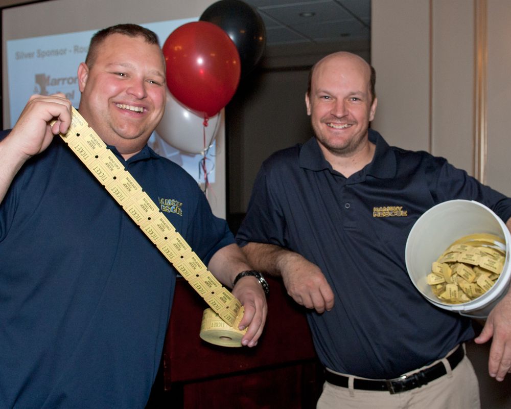 Two staff members in matching uniforms display a measuring stick and bowl of chips.