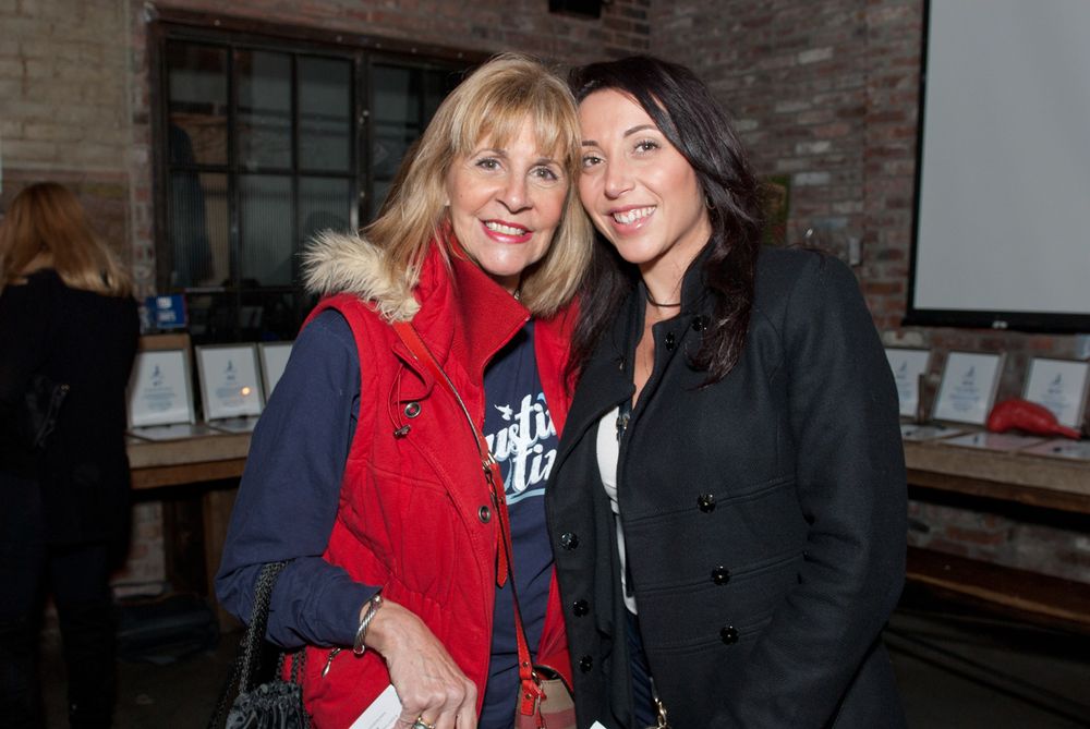 Two friends pose together at a brick-walled venue during an event.