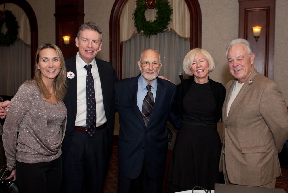 Five people posing together at an evening event with a holiday wreath visible in the background.