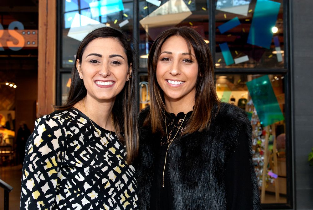 Two women in stylish outfits smiling at a social gathering.
