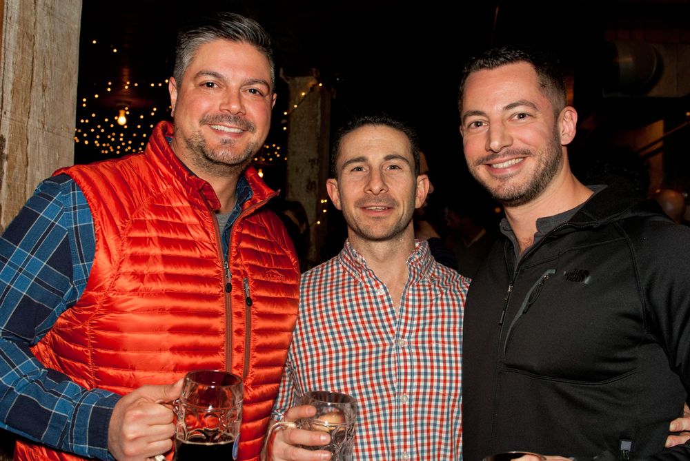 Three friends enjoying drinks together at a festive bar with string lights.