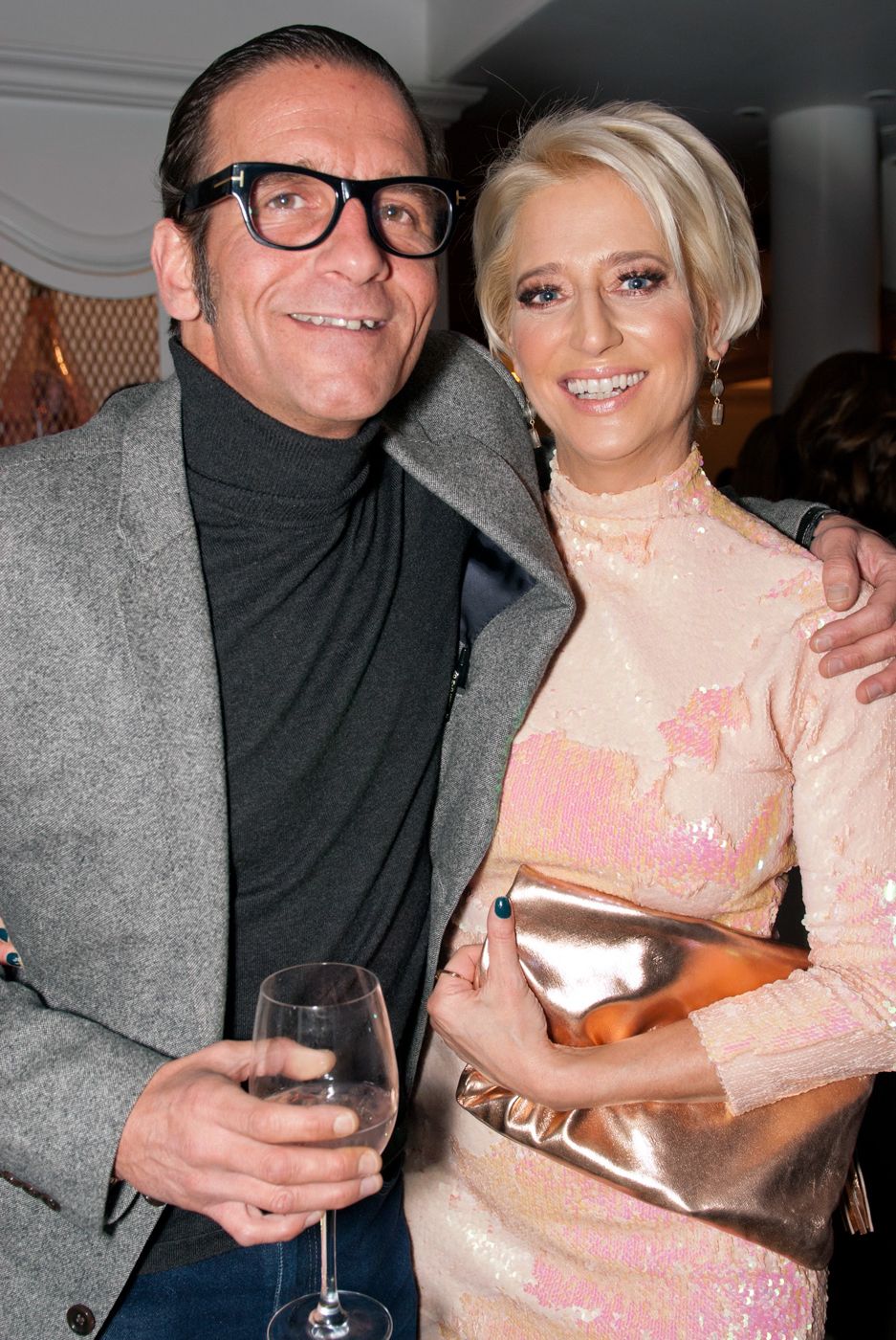 A couple in elegant evening attire holding drinks at an upscale event.