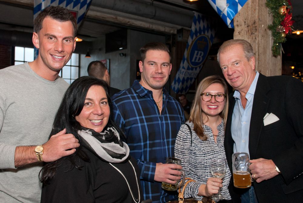 Group of five people enjoying drinks and conversation at a casual gathering with festive decorations.