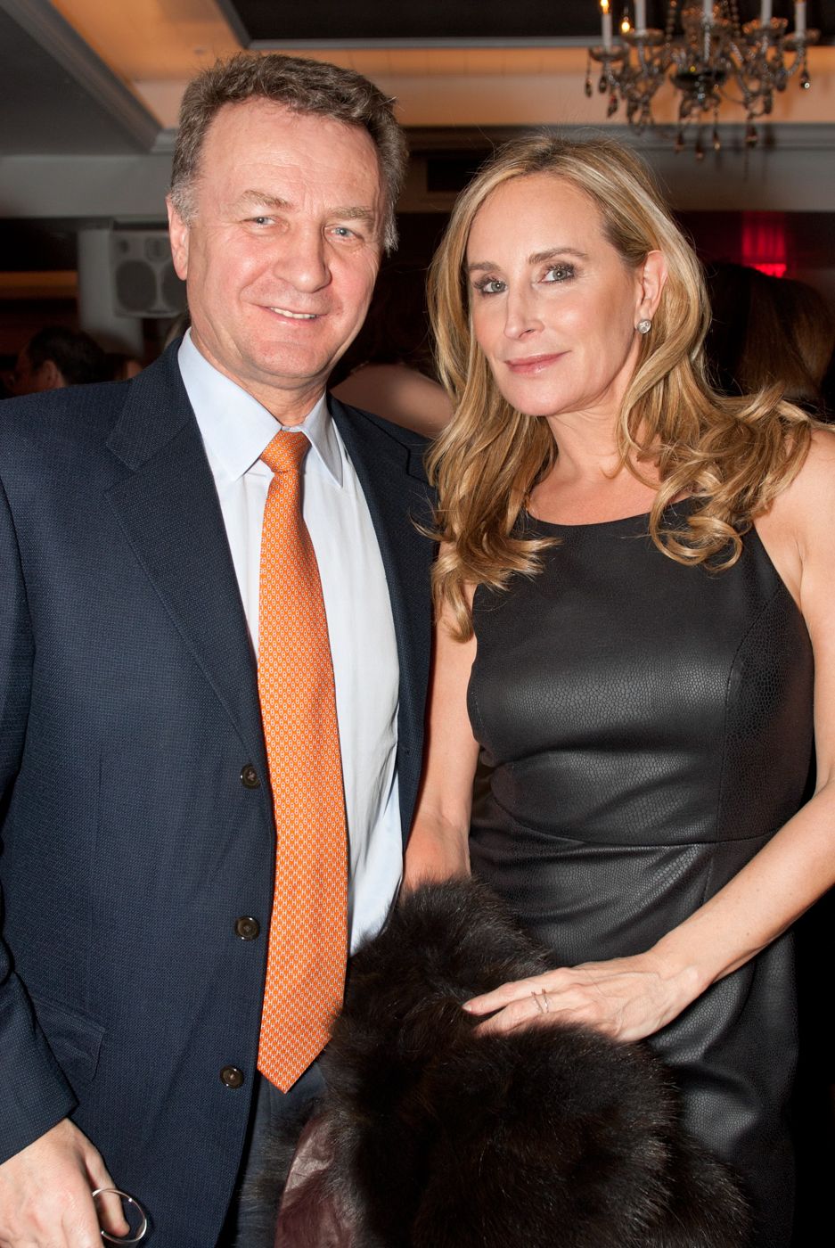 Couple in formal attire posing at an elegant event with a chandelier in the background.