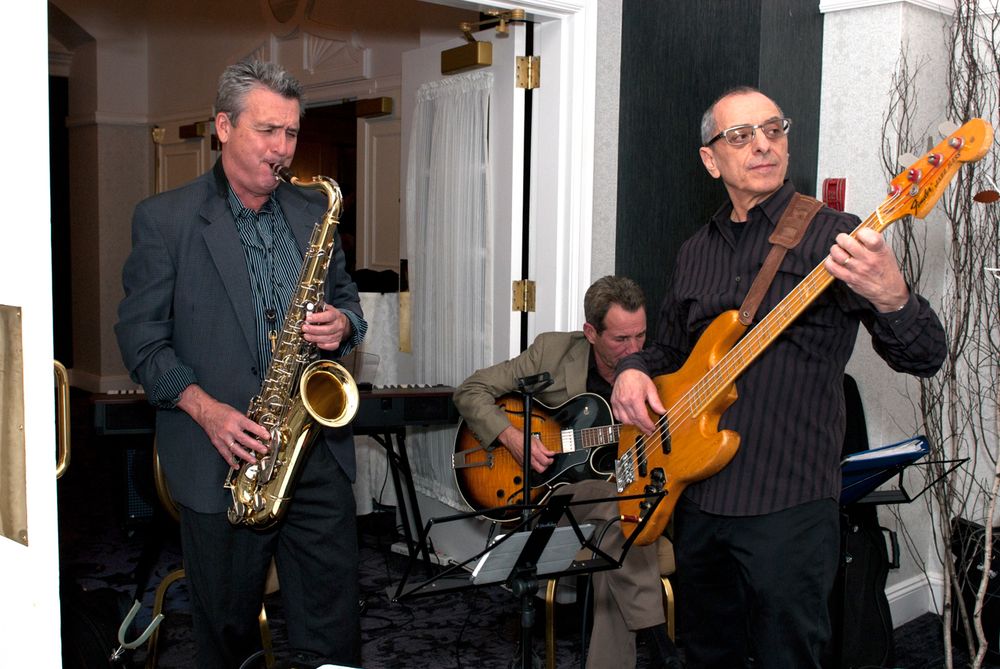 Musicians performing with saxophone and bass guitar during indoor event.