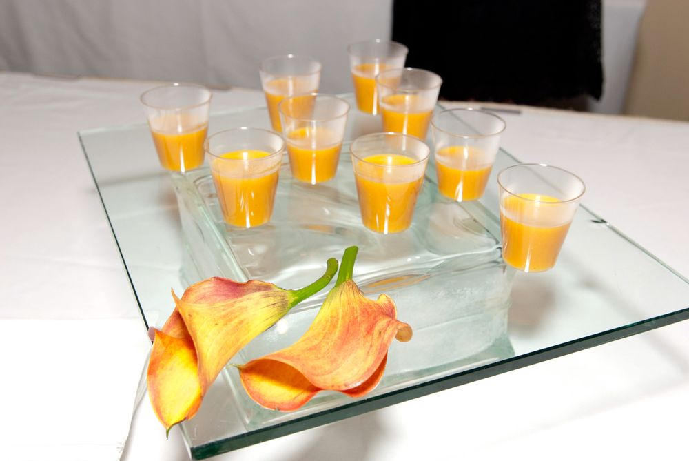Orange calla lilies and small glasses of orange juice arranged on glass serving tray.