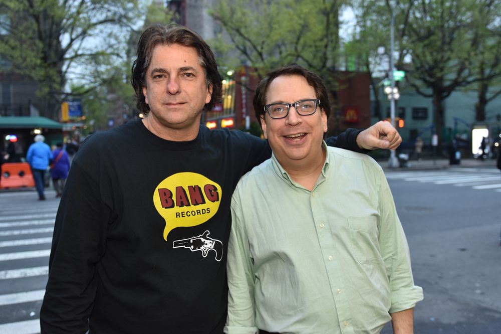 Two people pose outdoors on a city street, one wearing a BAND sweatshirt.