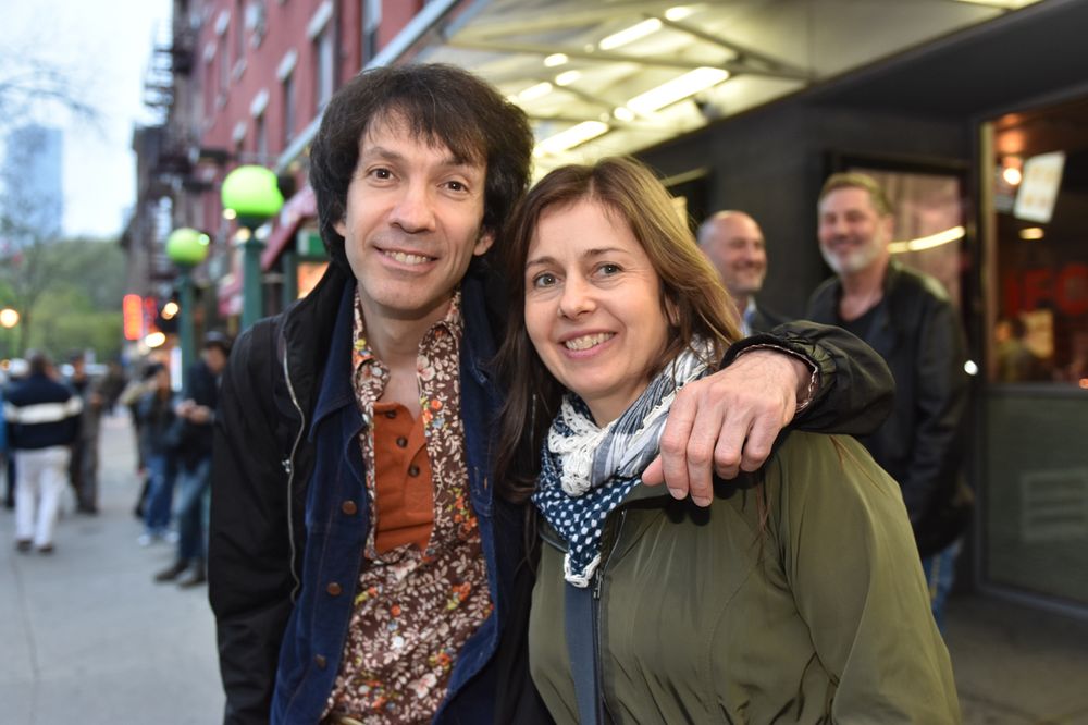 A couple poses together on a city sidewalk with storefronts in the background.