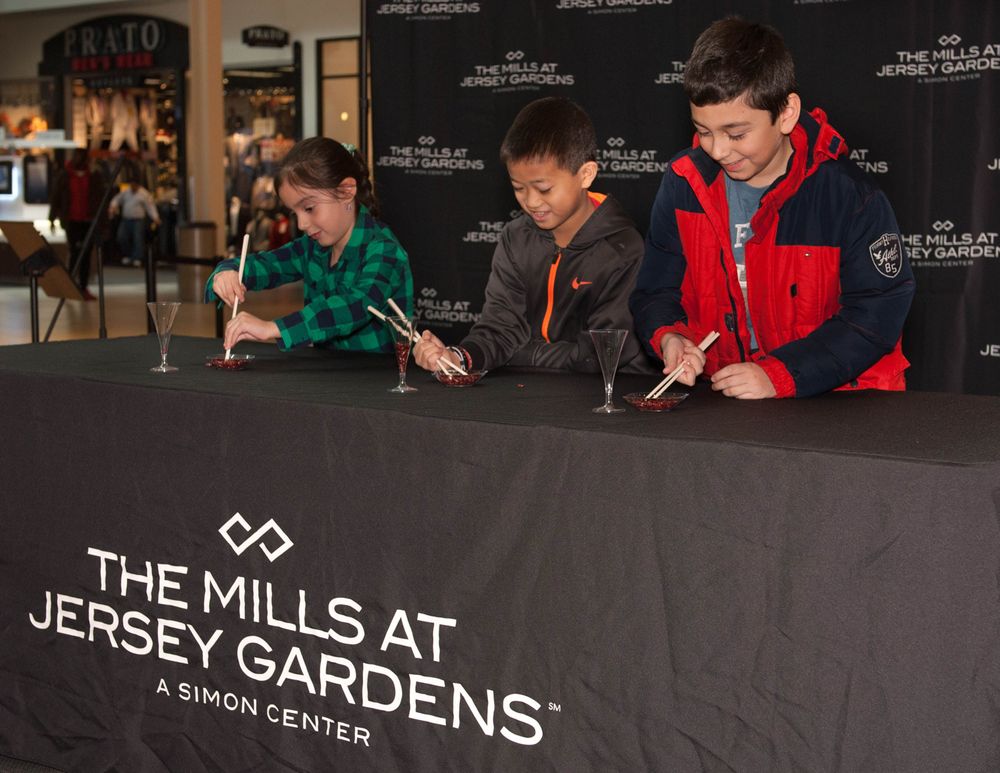 Young people sit at a signing table with The Mills at Jersey Gardens banner.