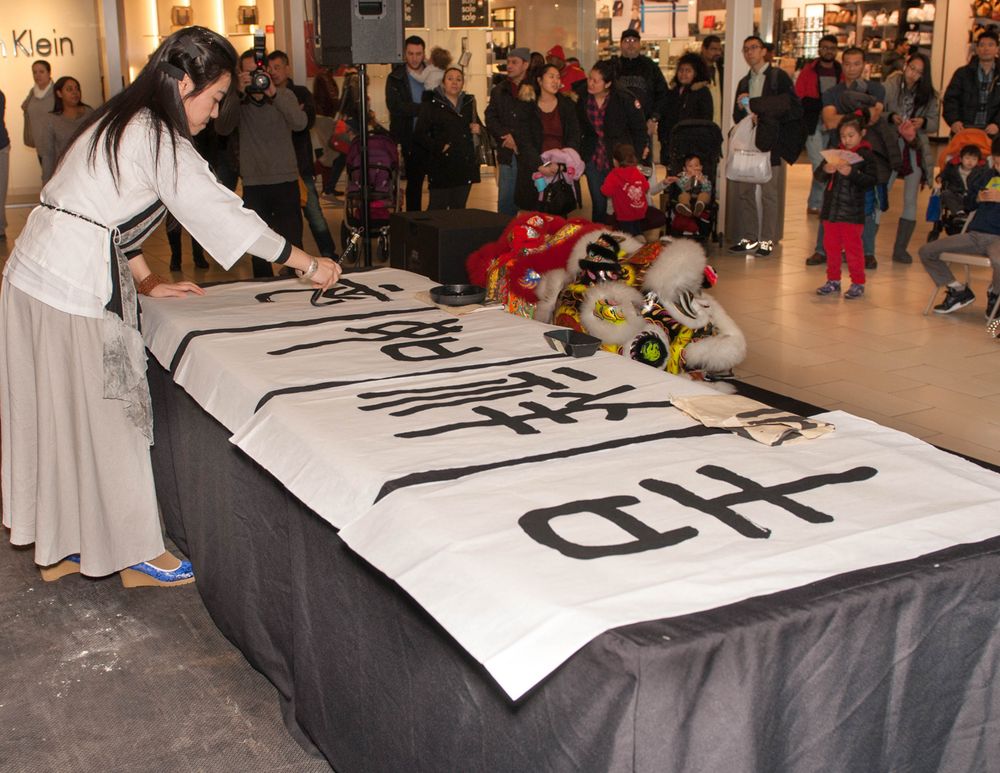 Person in light clothing writes on a large banner at a public event.