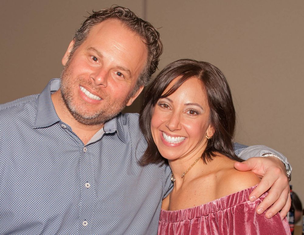 A couple smiles together at a social event while embracing.