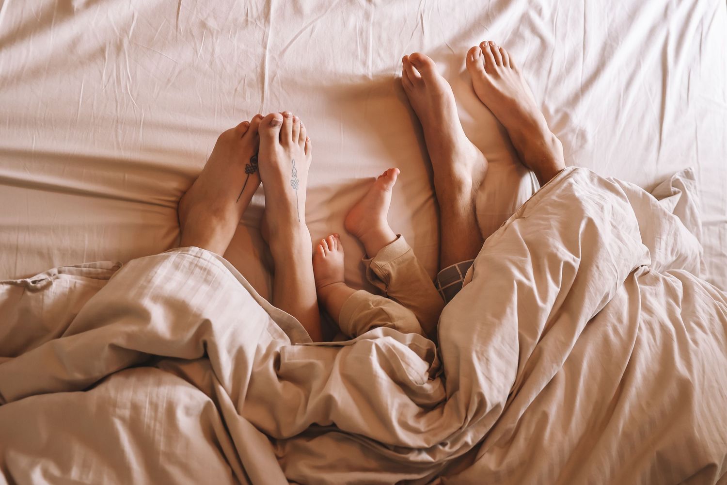 Feet peeking out from under cozy beige bedding in morning light.