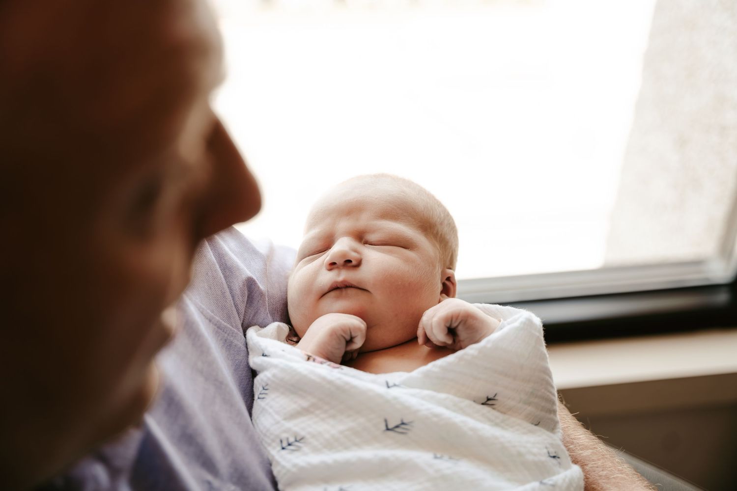 Peaceful sleeping newborn wrapped in patterned blanket by window at fresh 48 session