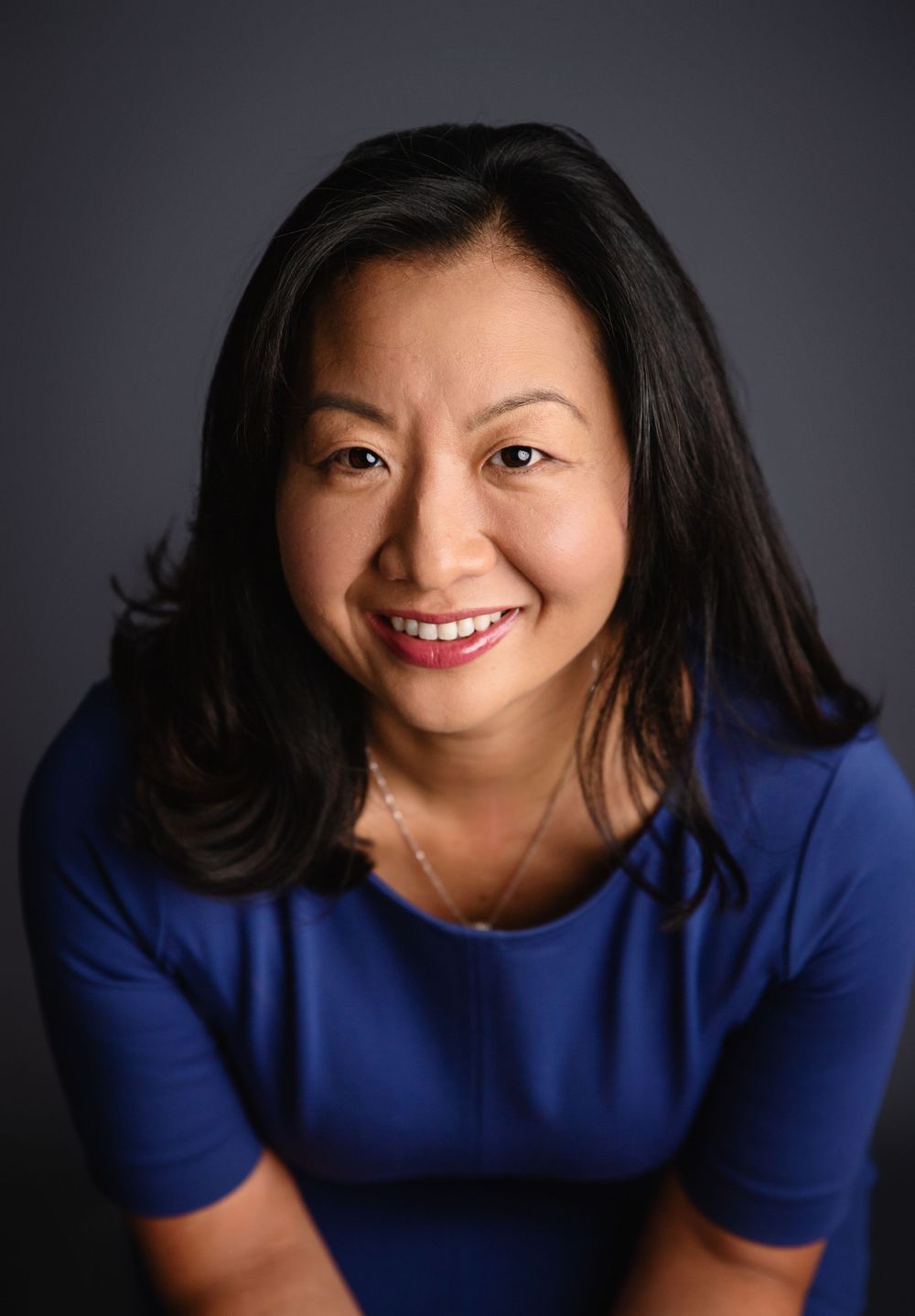 Professional portrait of a woman in a vibrant blue top smiling warmly against a dark background.