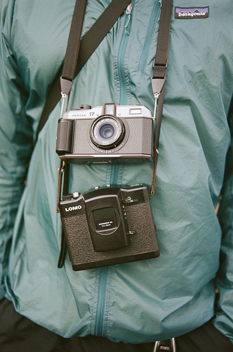 Two vintage cameras hanging on straps against a teal Patagonia jacket background.