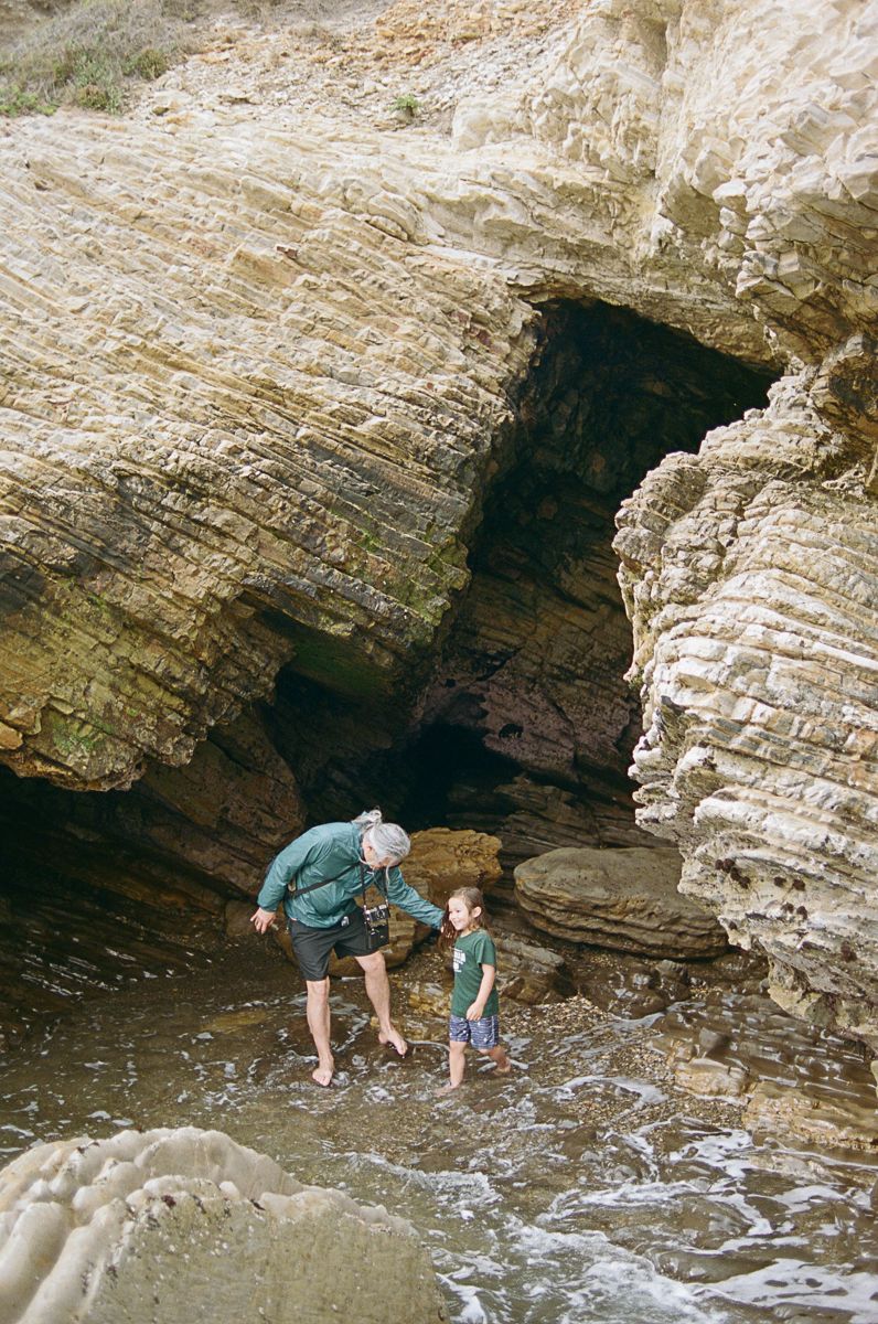 Two people exploring rocky coastal caves and tide pools along a rugged shoreline.