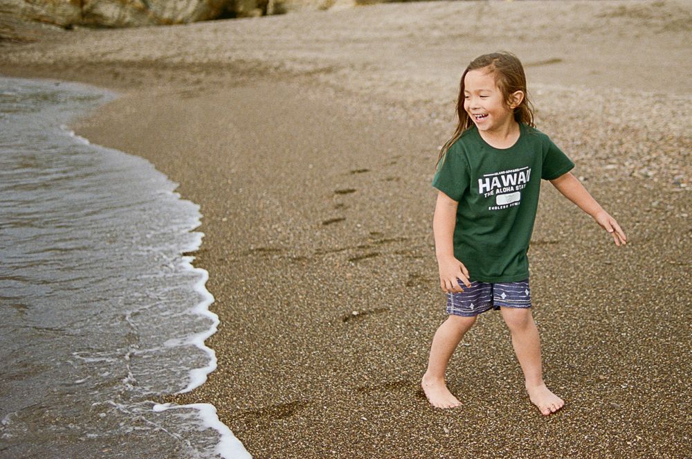 Small child playing at the ocean's edge on a sandy beach.