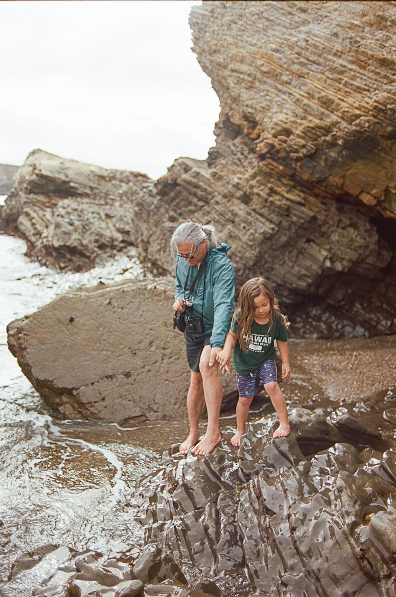 Two people exploring rocky coastal formations during low tide at the beach.