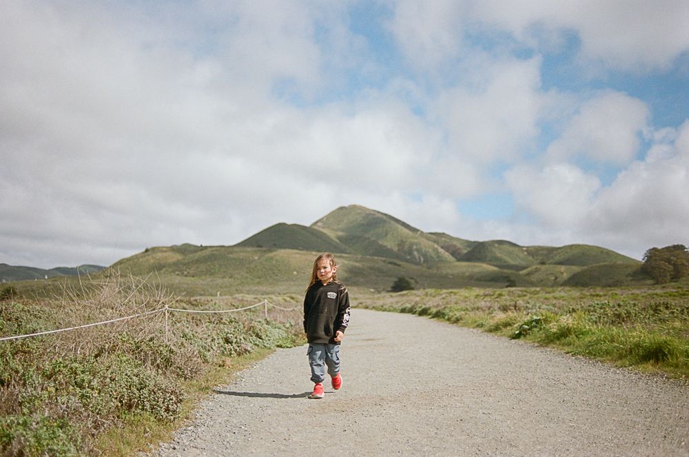 A winding path leads through green hills under cloudy skies.