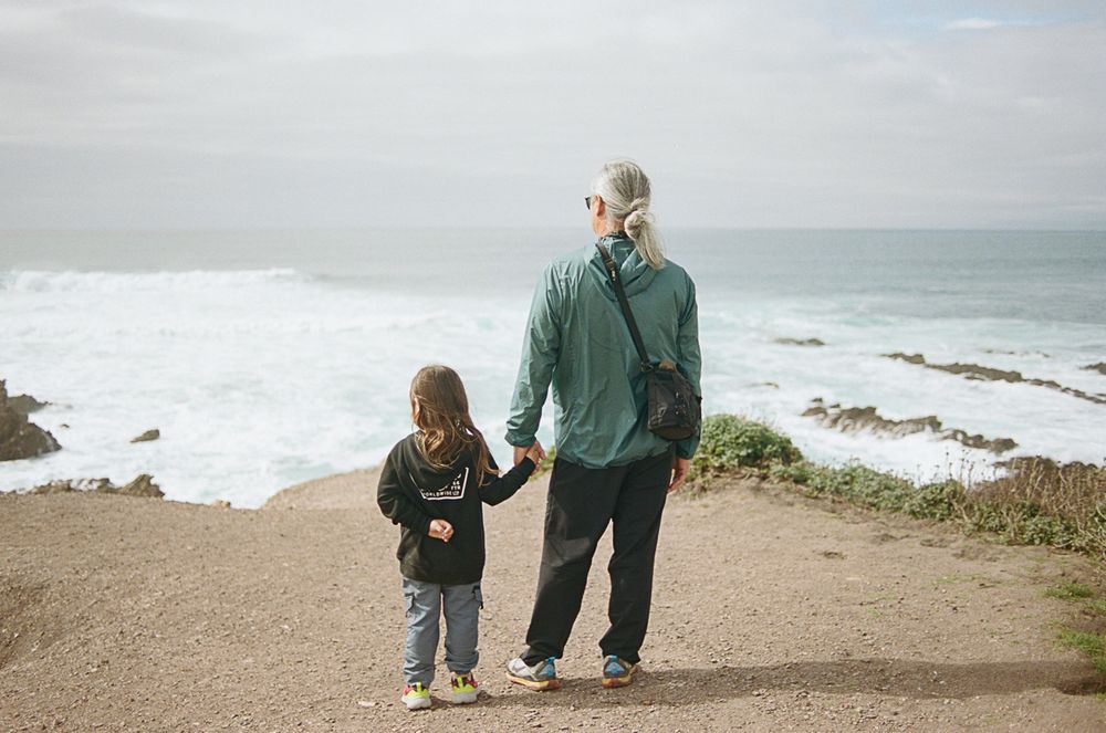 Two people walk along a coastal path overlooking the ocean.