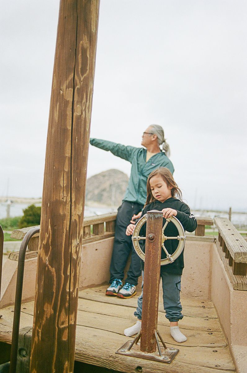 Two people playing on wooden pier with ship's wheel and coastal views.