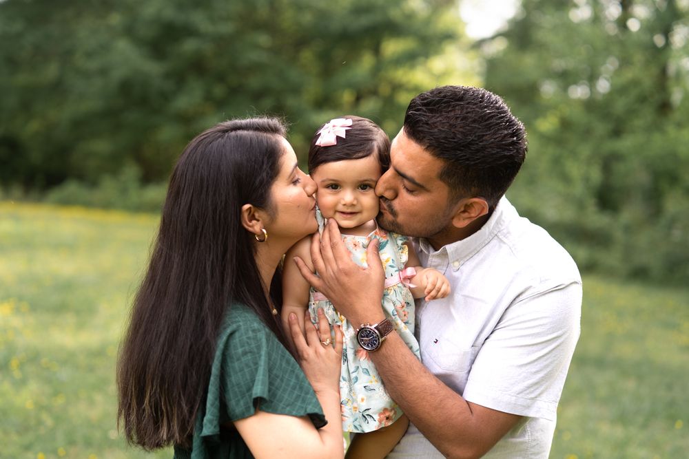 A mom and dad with their 11 month old daughter giving her kisses on her cheek
