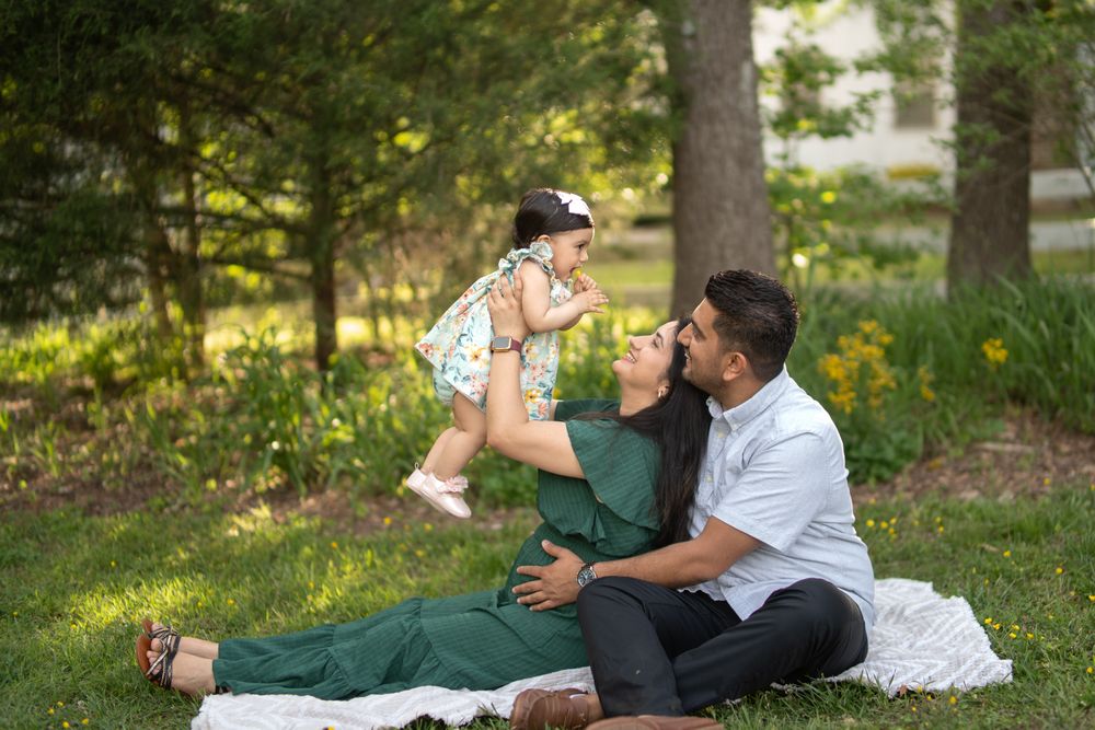 A mom and dad with their 11 month old daughter sitting in the grass