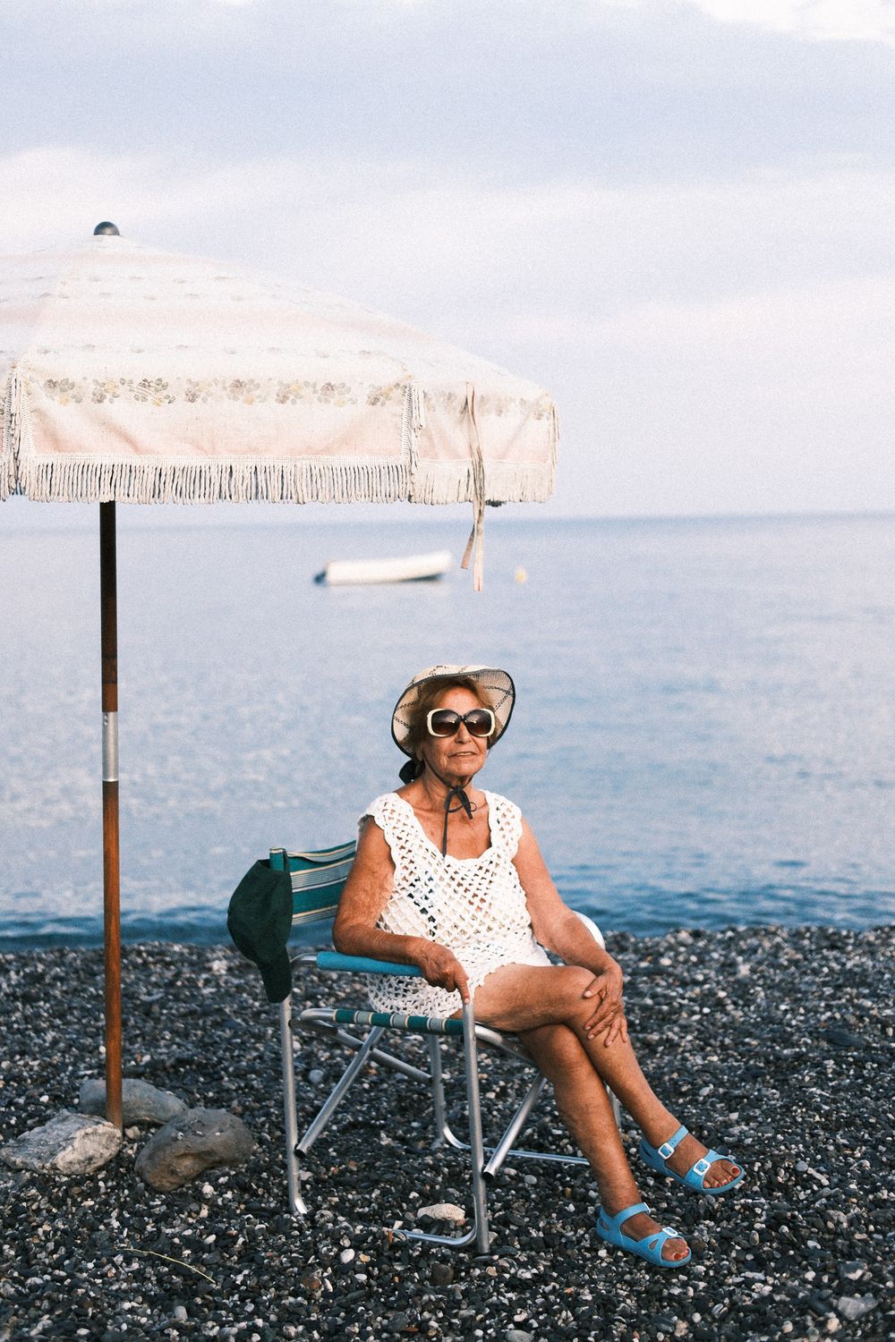 Elderly woman sitting on a rocky beach under an umbrella