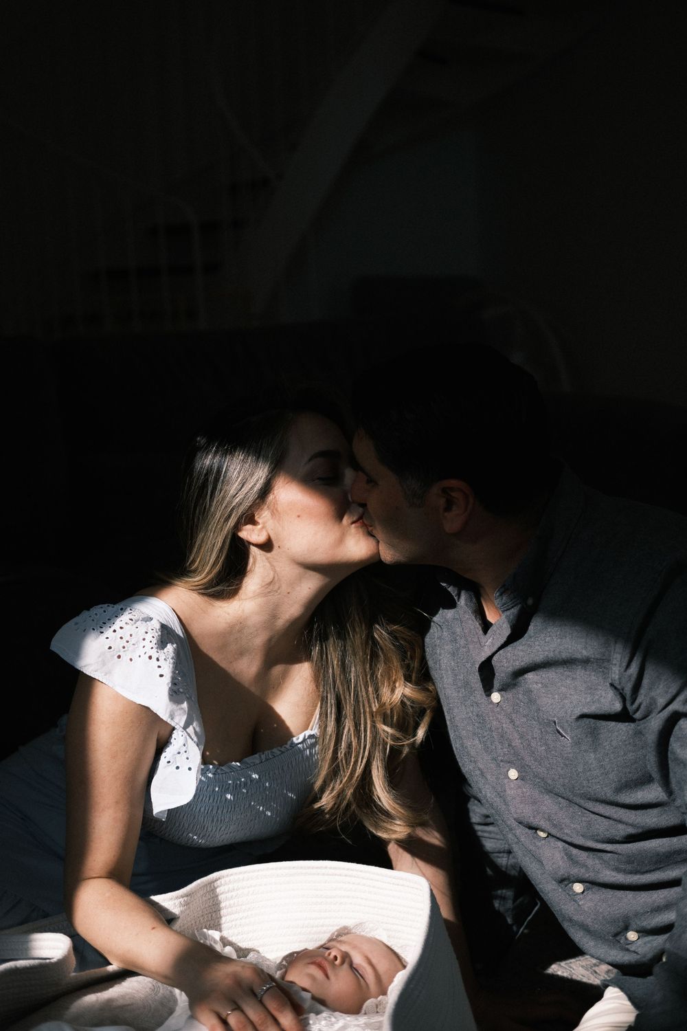 couple kissing portrait session with sleeping baby in a bassinet