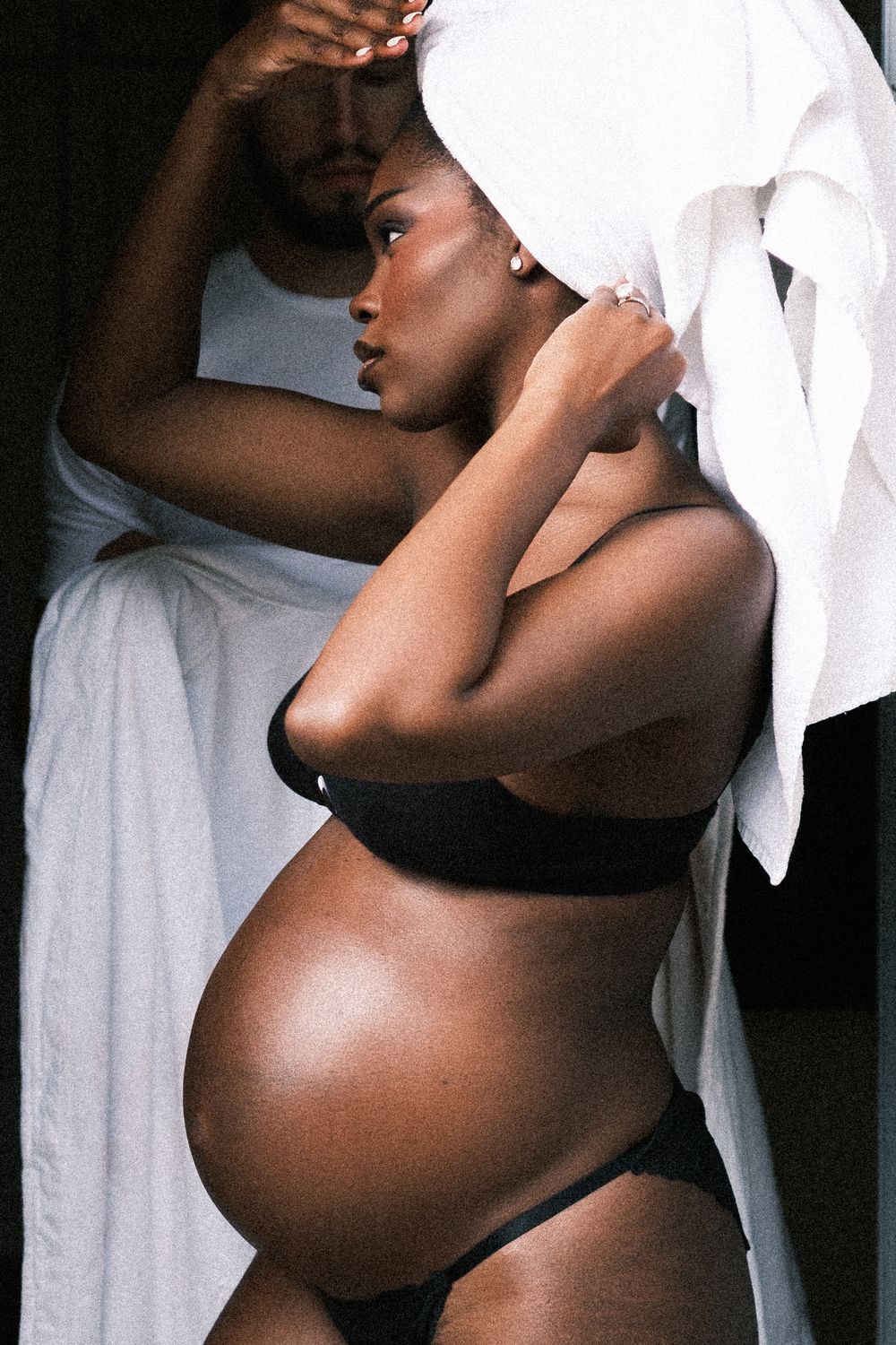 Pregnant woman in black lingerie with white towel on head posing gracefully during maternity photoshoot.