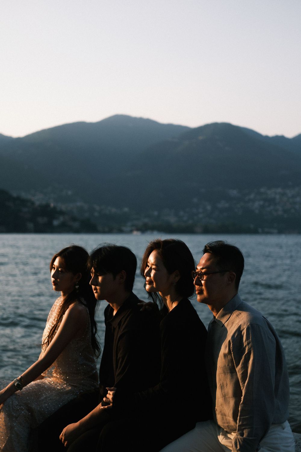 Four people sit in profile by a mountain lake at dusk, bathed in soft golden light.