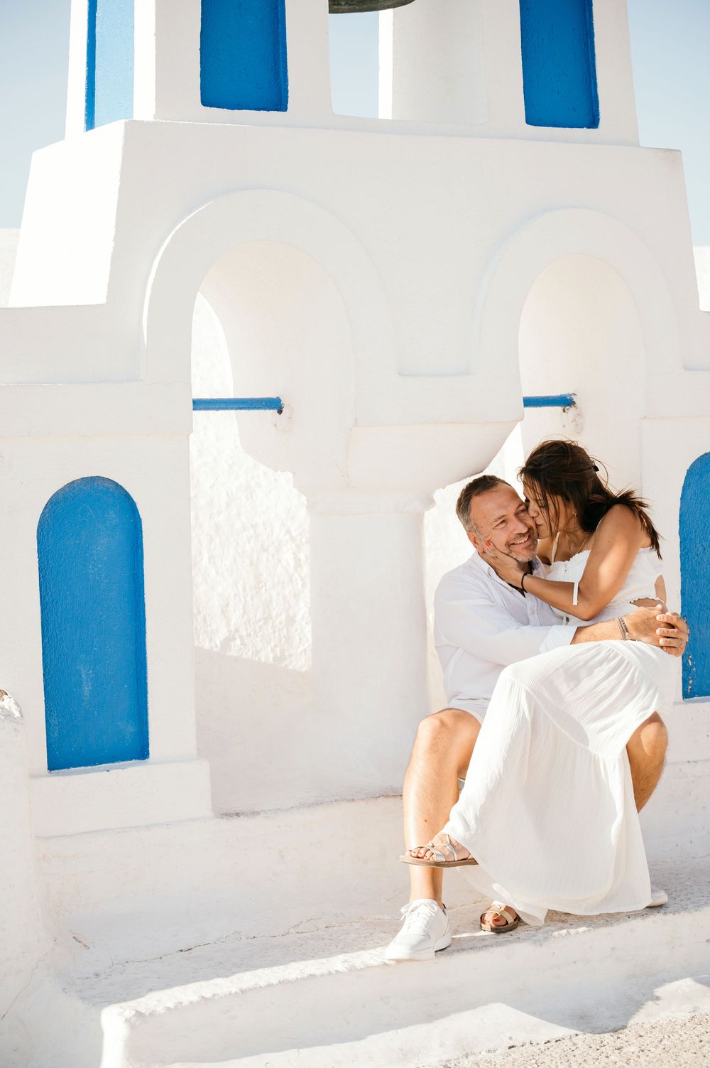 Romantic embrace on white church steps with traditional blue Cycladic architecture.