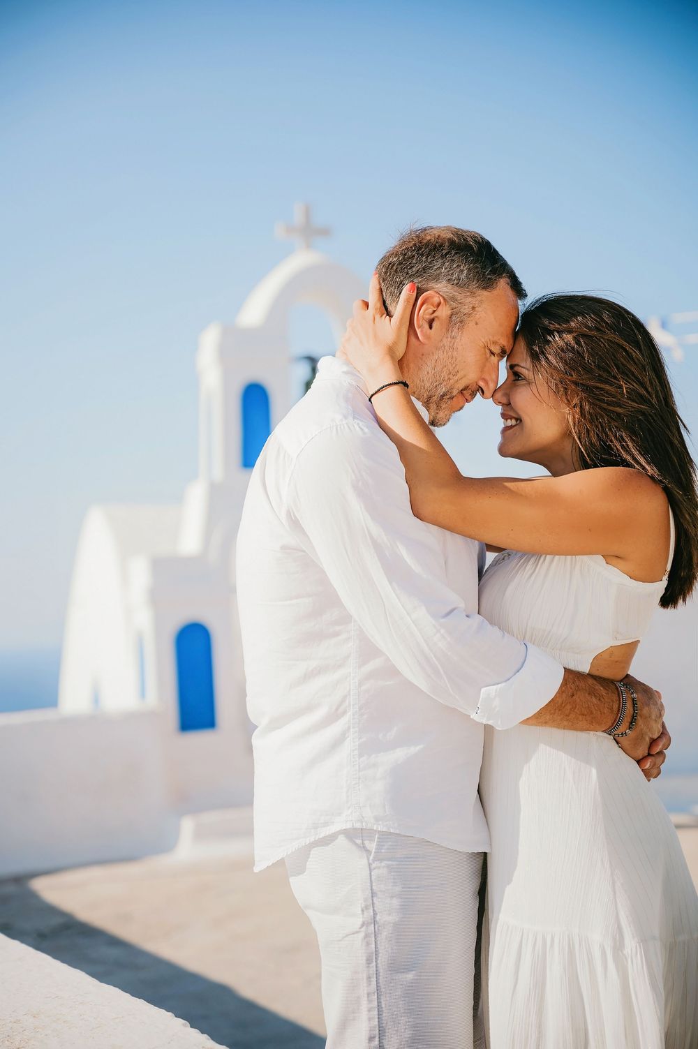 Intimate moment between couple in white against classic Greek church architecture.