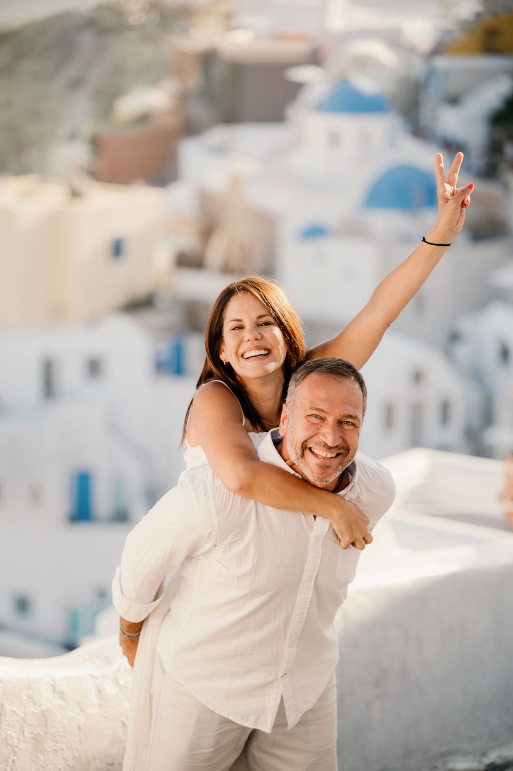 A joyful moment captured against the white buildings of Santorini, Greece with a peace sign gesture raised high.