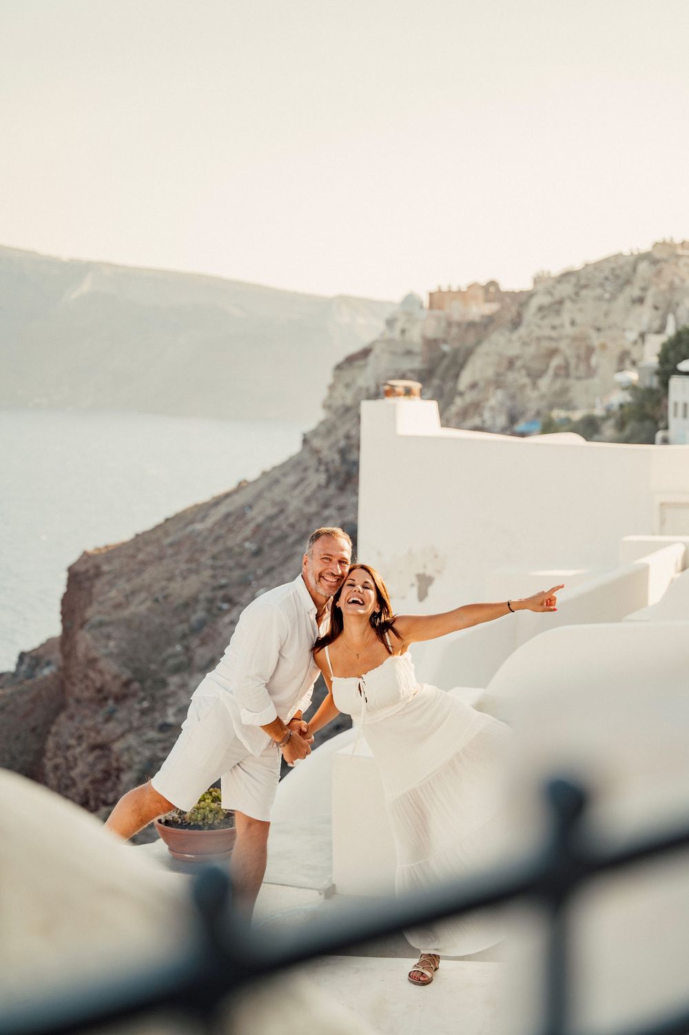 A romantic couple pose playfully on a white terrace overlooking the Aegean Sea in Santorini.